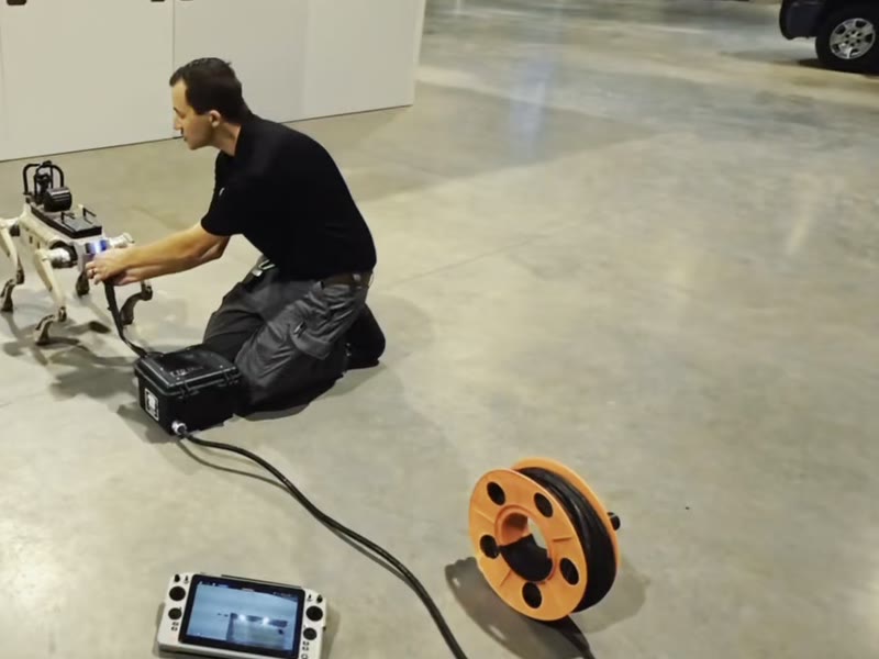A team member kneeling to connect equipment to the robot, with the controller and a cable reel on the floor